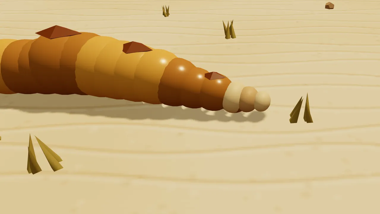 A close-up of the end of Sandy’s tail lying on pale rippled sand: golden body beads with darker brown bands and small brown diamond-shaped bumps on top, ending in a rattle of three round beads, cream, tan and cream, with spiky tufts of dry desert grass and a small pebble around it